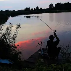 Wędkarz łowiący na feeder przy zachodzie słońca nad jeziorem.