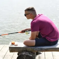 Chłopak z wędką na drewnianym pomoście. Czy wędkarstwo to sport? Cierpliwość i skupienie, które tu widać, sugerują, że tak.