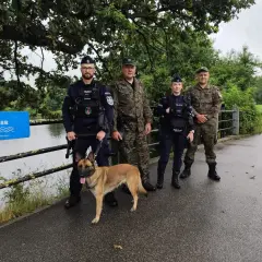 Funkcjonariusze z psem patrolują teren nad wodą. To część działań społecznej straży rybackiej.