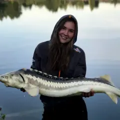 Uśmiechnięta wędkarz trzyma imponującego jesiotra. To był udany zestaw na jesiotra!