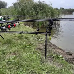 Wędki ustawione nad wodą, z widocznymi kołowrotkami i trzcinami w tle.