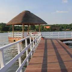 Drewniane molo prowadzi do altany nad wodą. W tle las i budynki. Zalew w Siemiatyczach zaprasza do wypoczynku.