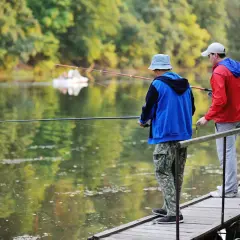 Dwóch mężczyzn łowi ryby z drewnianego pomostu na spokojnym jeziorze.