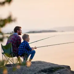 Ojciec i syn łowią ryby na brzegu jeziora o zachodzie słońca.