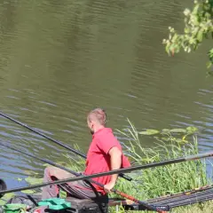 Dwóch wędkarzy łowi ryby nad wodą. Jeden z nich wyciąga sieć z rybą. W tle widać drzewa i roślinność. Wody polskie właściciel.