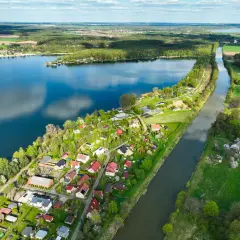 Malownicze pławniowice jezioro otoczone zielenią i domkami letniskowymi. Woda odbija chmury, a kanał przecina krajobraz.
