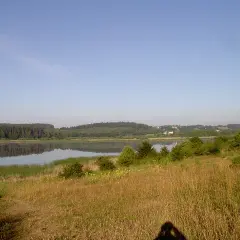 Spokojne jezioro kielarskie odbija las i niebo. Na pierwszym planie trawiasty brzeg.