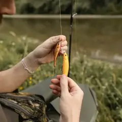Wędkarz przygotowuje przynęty do spinningu. Dwie błyszczące rybki, jedna pomarańczowa, druga złota, wiszą na żyłce.