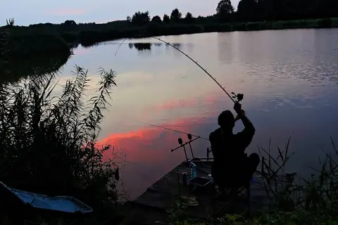 Wędkarz łowiący na feeder przy zachodzie słońca nad jeziorem.