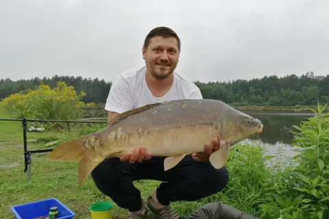 Mężczyzna trzyma dużą rybę karpia na tle jeziora i lasu.