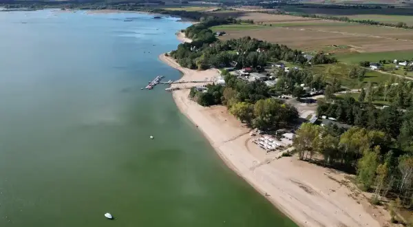 Piękny dzień nad Mietkowym zalewem. Piaszczysta plaża, łodzie na wodzie i zielone drzewa tworzą idealne miejsce na wypoczynek.