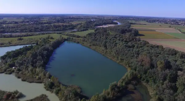 Widok z lotu ptaka na jezioro otoczone lasem, w tle pola i rzeka.