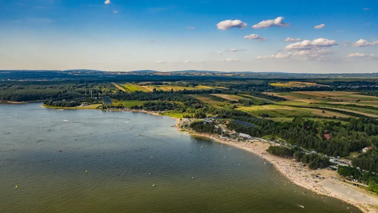 Widok z lotu ptaka na zalew Chańcza z piaszczystą plażą pełną ludzi, zielonymi lasami i polami w tle.