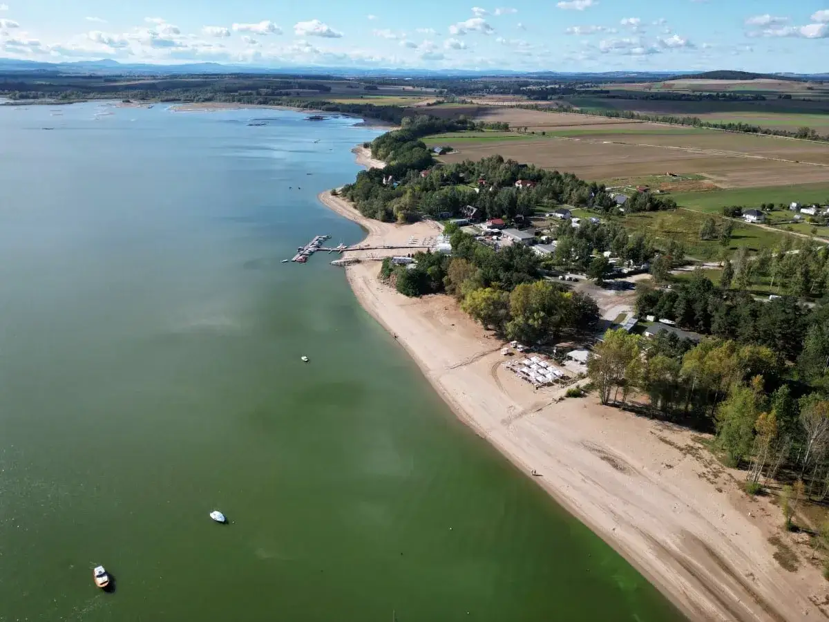 Widok z lotu ptaka na Zalew Mietkowski z piaszczystą plażą, mariną z łodziami i zielonymi polami w tle.