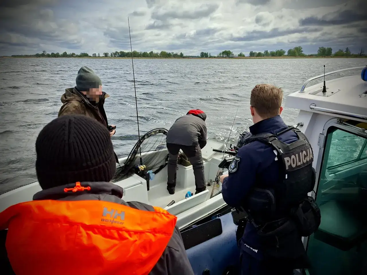 Policjant wypisuje mandat za brak karty wędkarskiej wędkarzowi na łodzi.