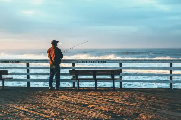 Mężczyzna z wędką na molo, cieszący się spokojnym dniem wędkarza nad wzburzonym oceanem.